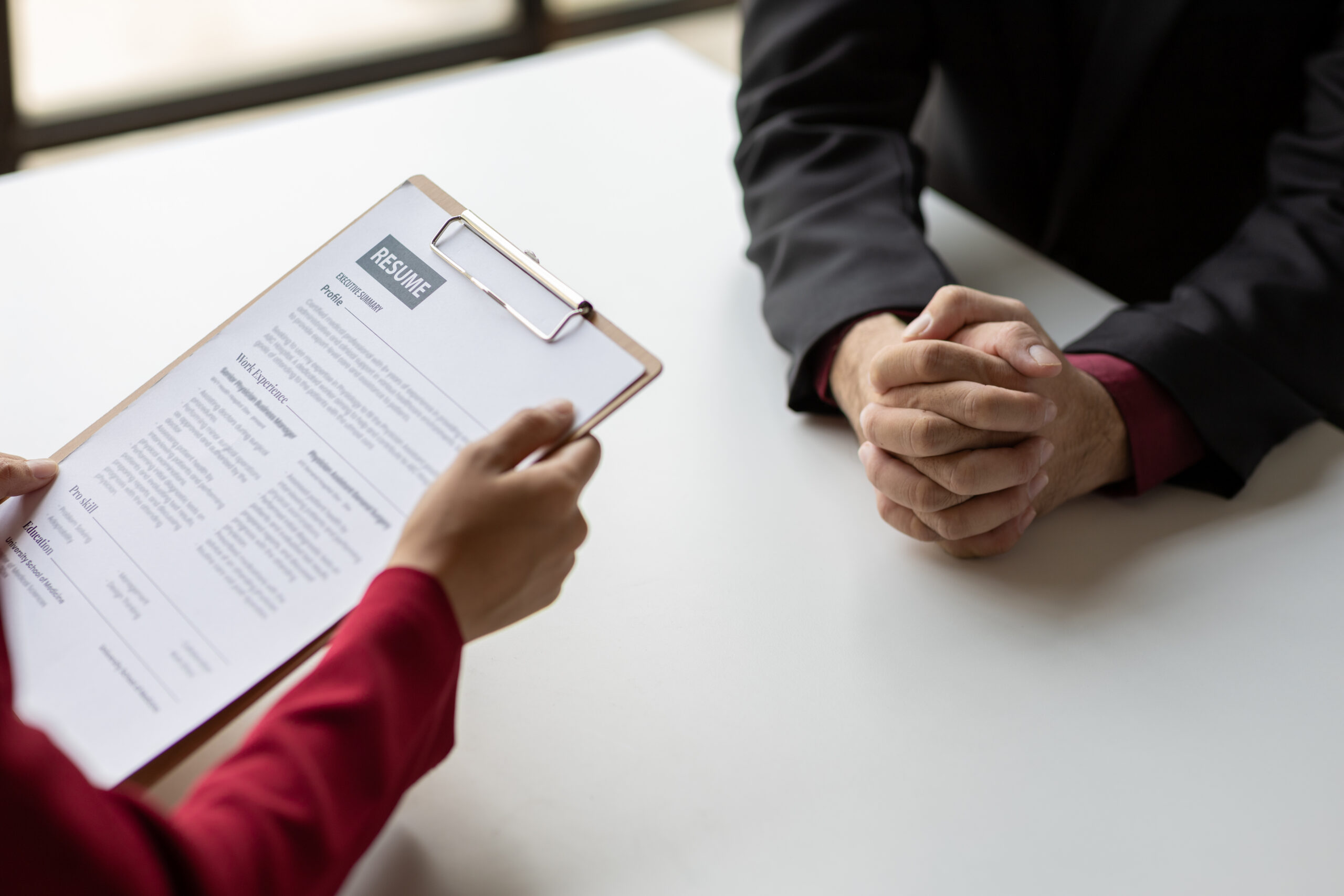 A top view of a business professional holding a resume on a clipboard with another individual sitting across the table.