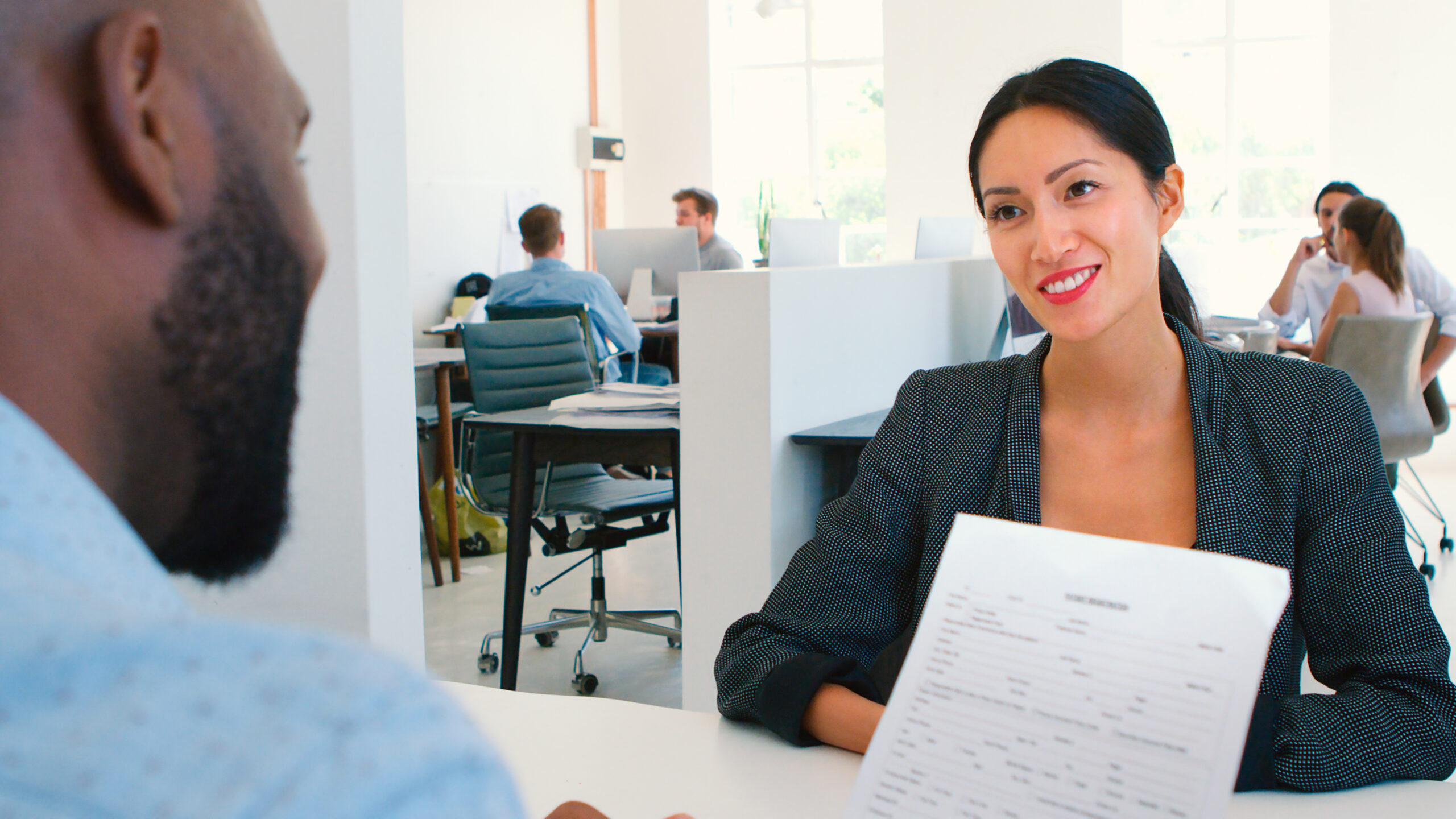 A young woman being interviewed in a bright, modern office setting, sitting across the hiring manager.